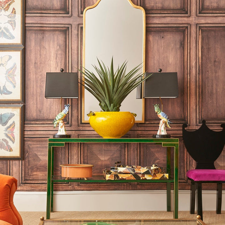 Decorative interior with a green console table, yellow vase, and mirror against a wooden paneled wall.