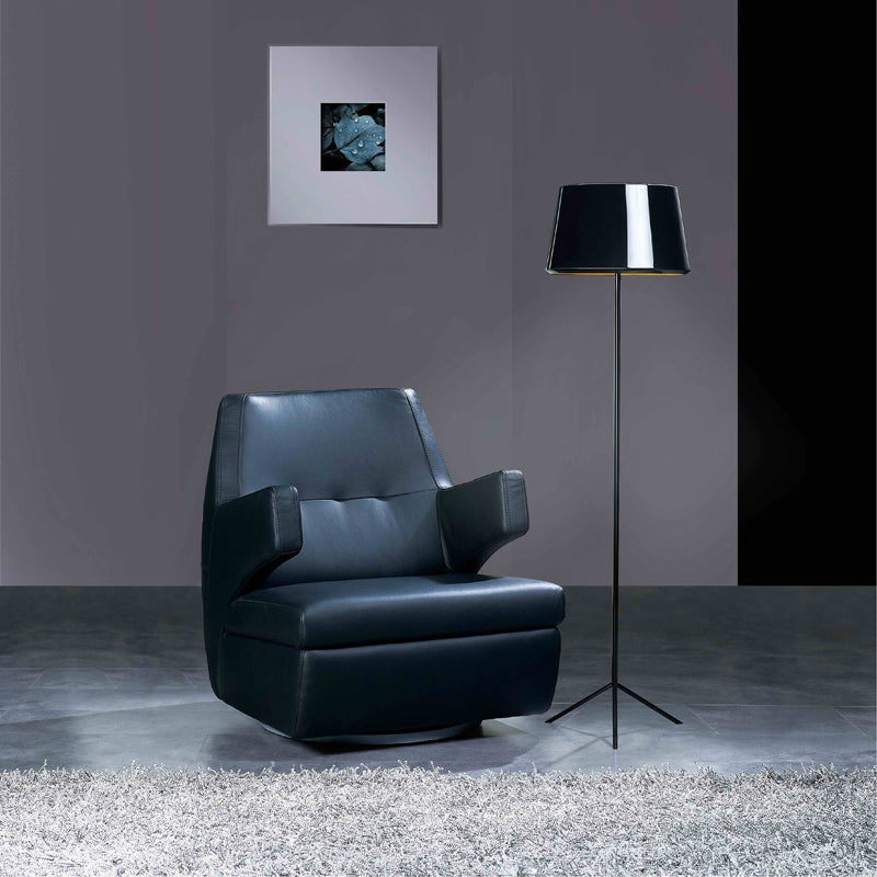 Modern black leather armchair in a room with a floor lamp and abstract painting on the wall.