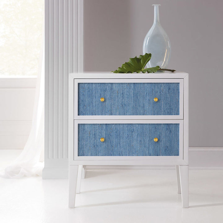 A white painted Costa Retro nightstand with blue drawers, placed against a neutral background with a decorative bottle on top.