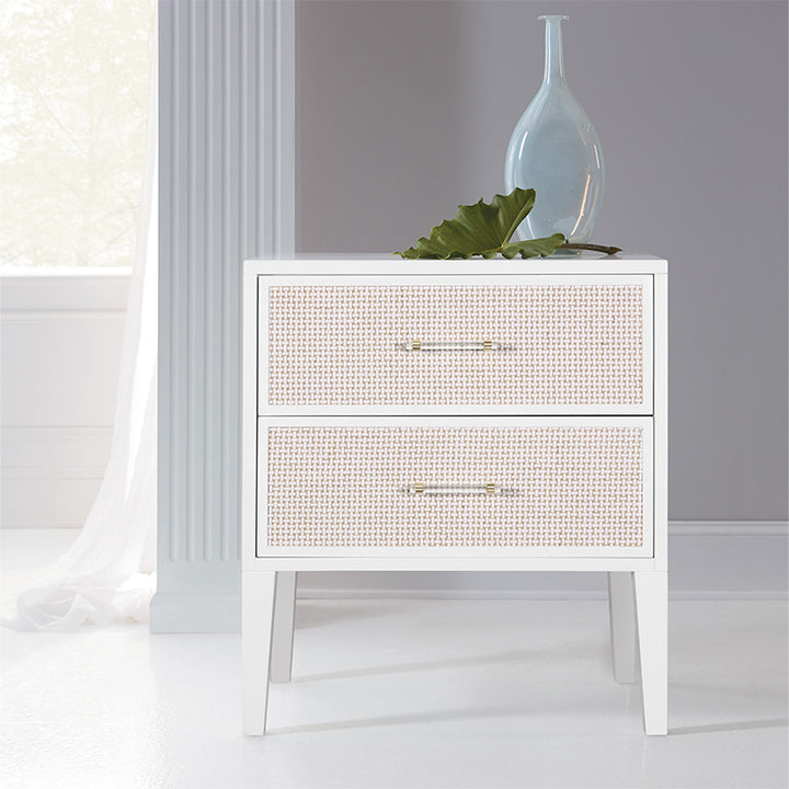 White nightstand with two drawers, decorative vase, and leaf on a light background