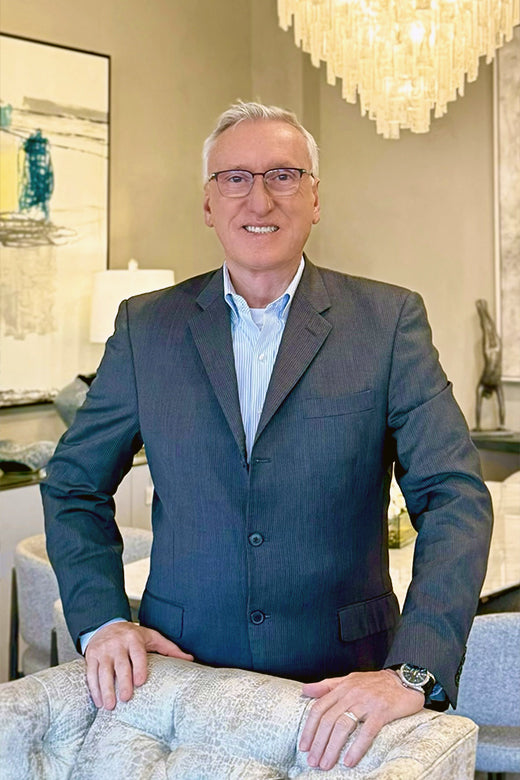 Man in a suit standing in an elegant room with a chandelier.